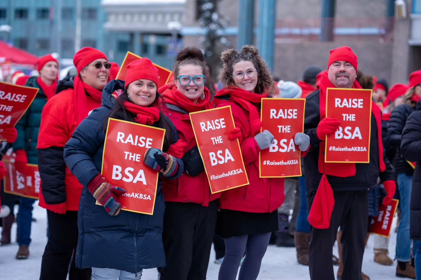 a group of educators dressed in red and holding signs smile together for a picture at a rally to raise the BSA