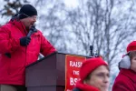 President Tom Klaameyer is dressed in red at the microphone at a rally.