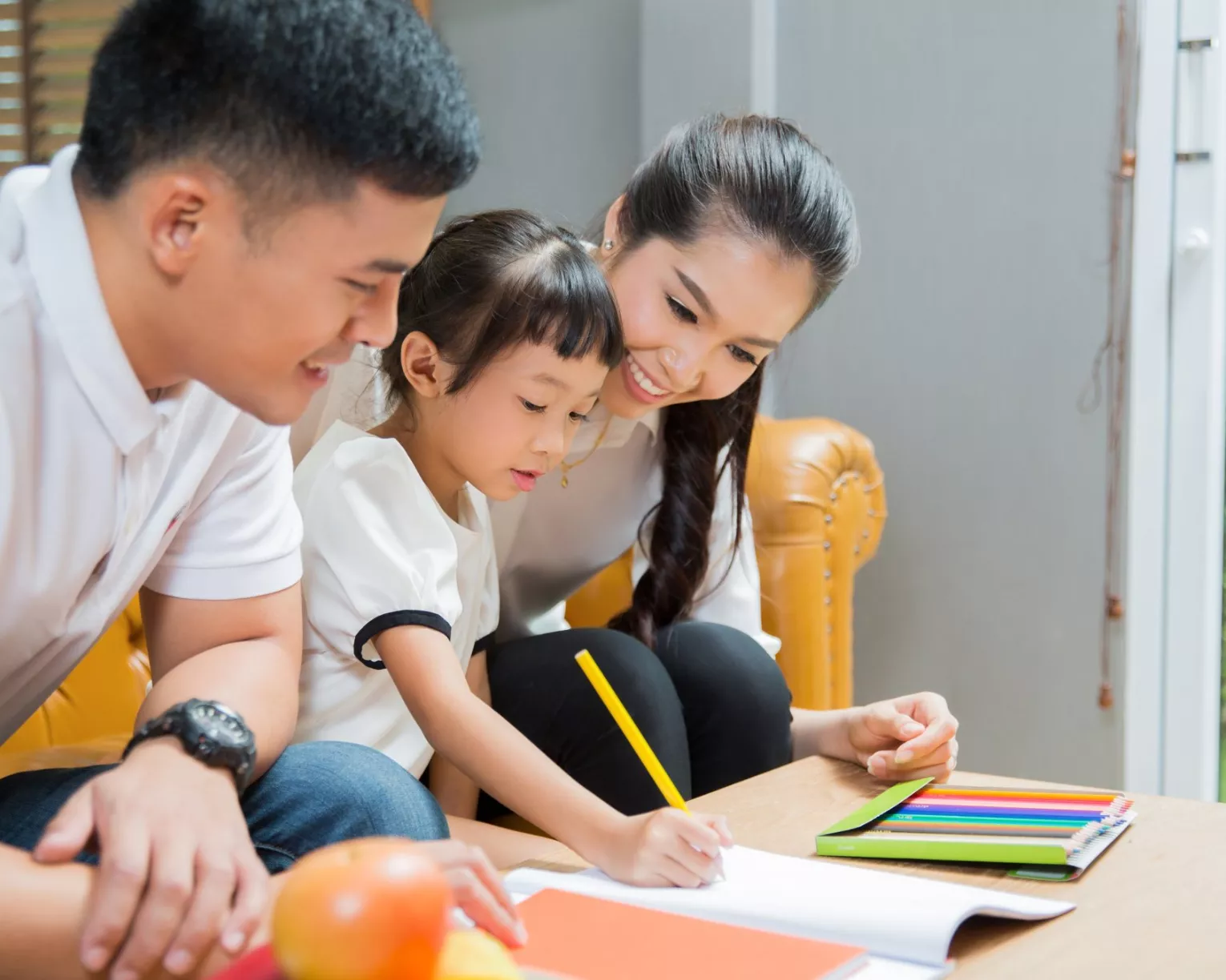 Two adult family members help a child write.