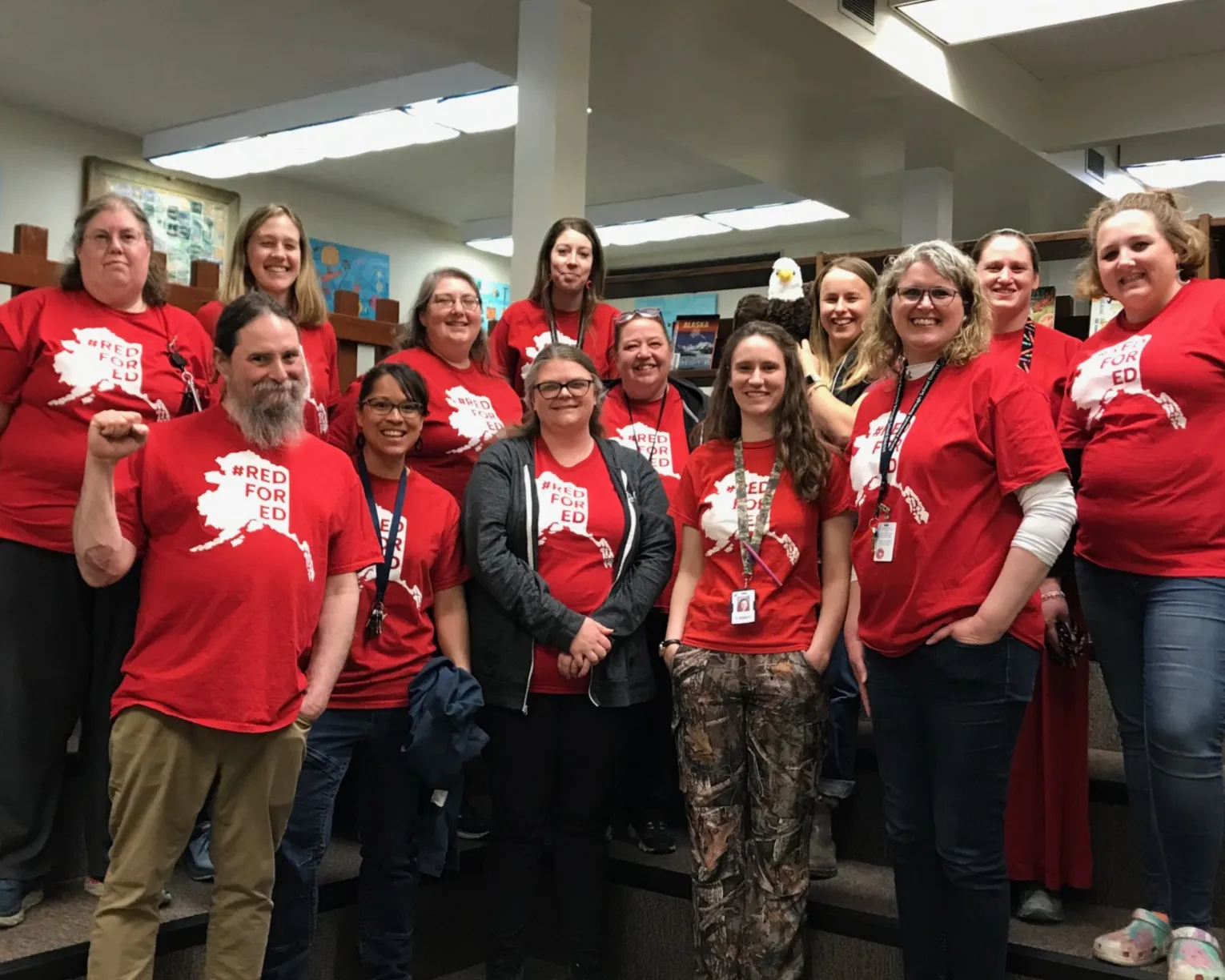 NEA-Alaska members wear red for ed as they pose with smiles in a school library.