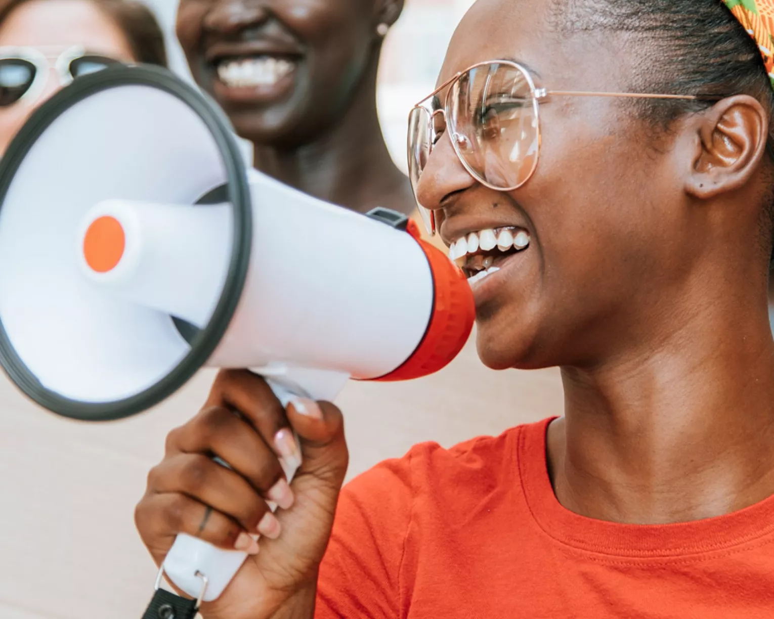 A young black woman holds a megaphone. She appears to be laughing. There are people behind her out of focus.