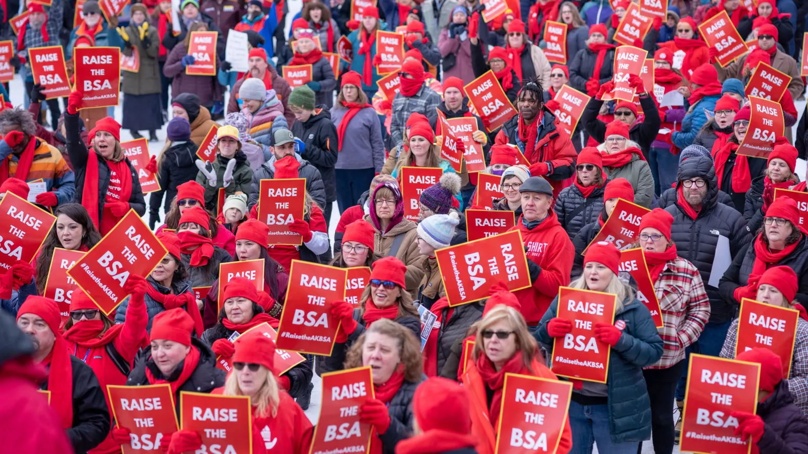 A sea of people in red rally in the street holding up signs that read "Raise the BSA".
