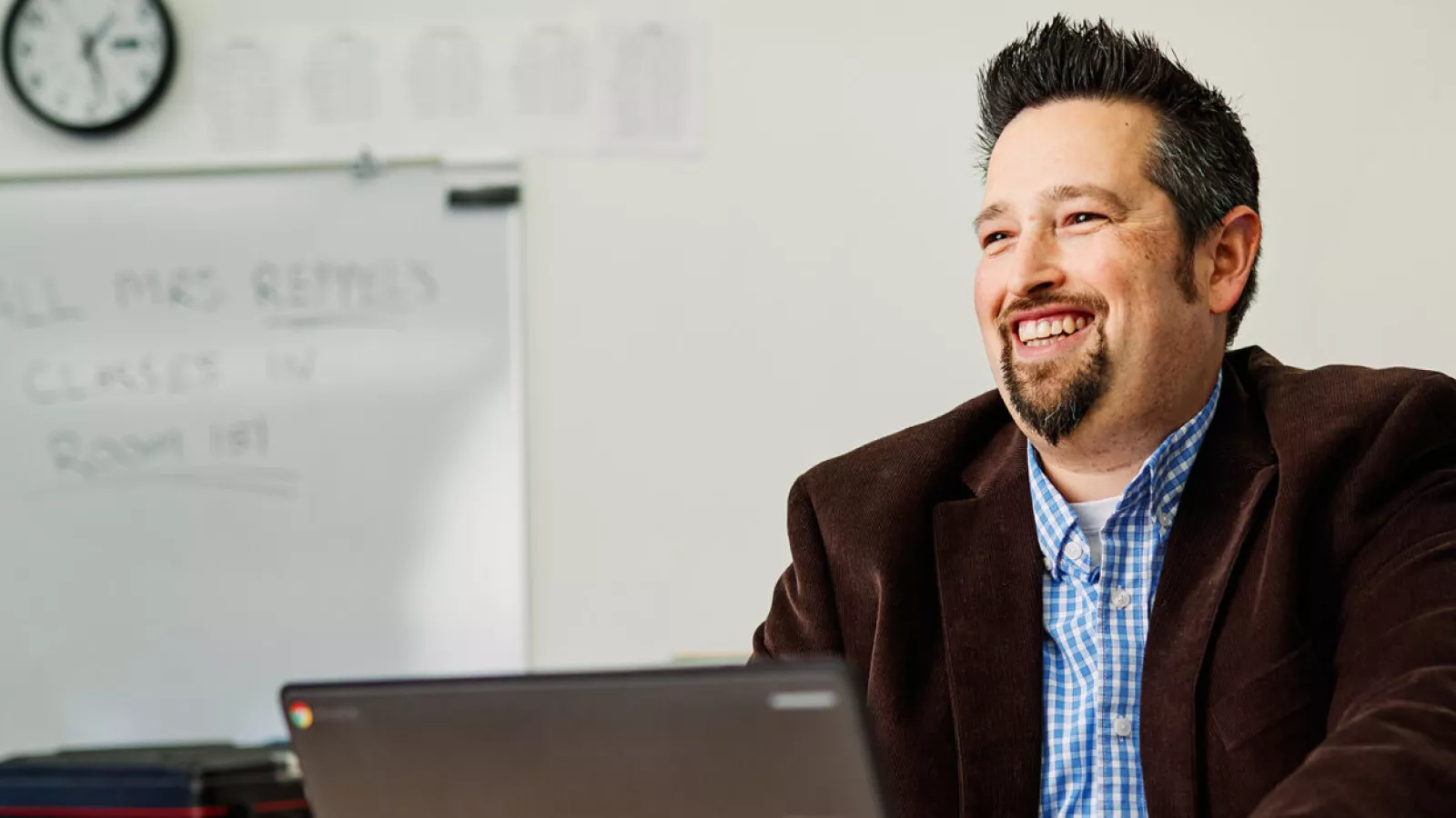 A white male educator with short brown hair and a beard sits at his computer smiling.