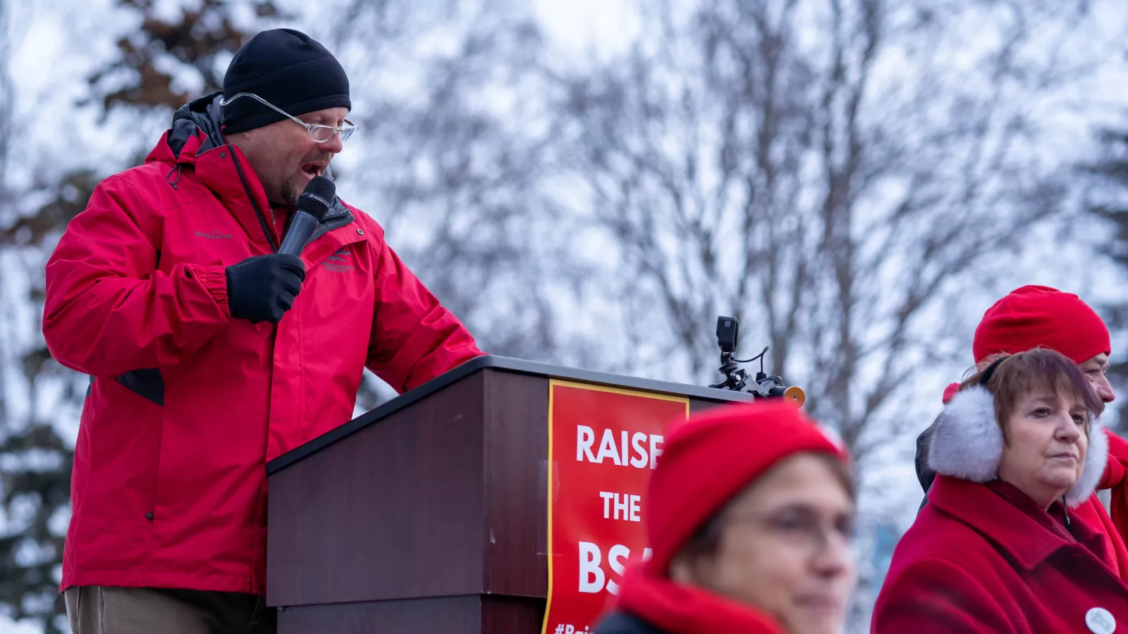 President Tom Klaameyer is dressed in red at the microphone at a rally.