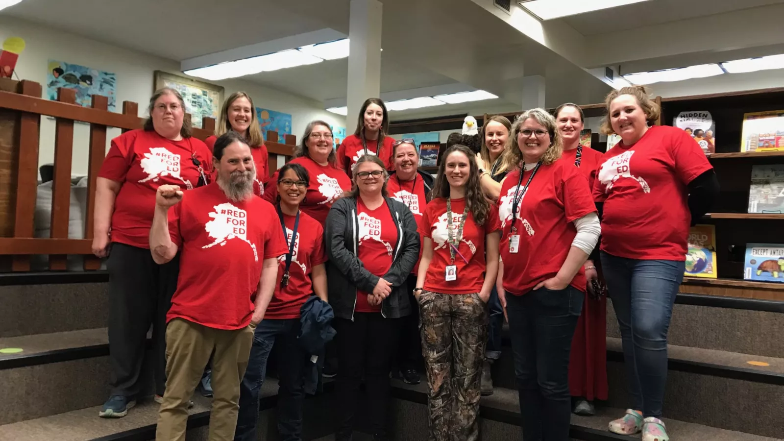 NEA-Alaska members wear red for ed as they pose with smiles in a school library.