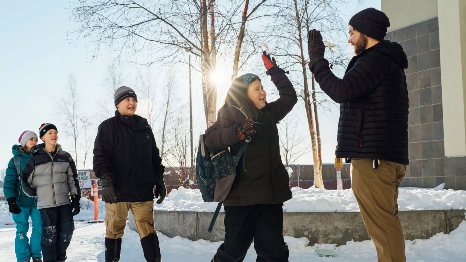 A teacher high fives a line of students in a wintery setting.
