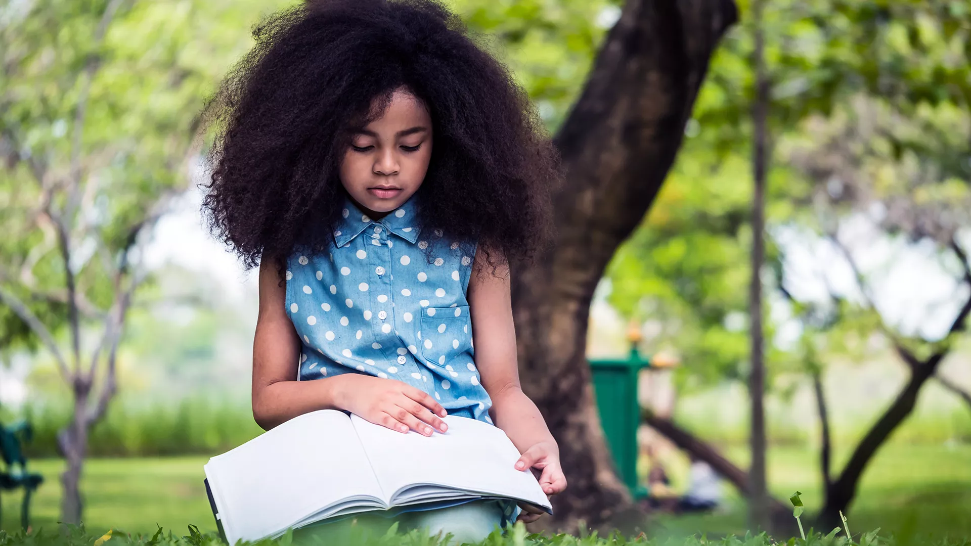 young girl reading book outside in summer