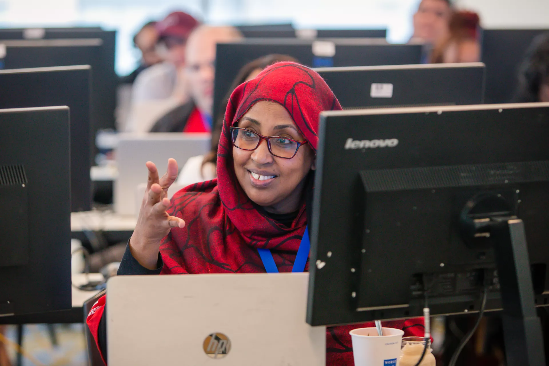 a photo of a woman wearing a red patterned hijab smiling in a computer lab