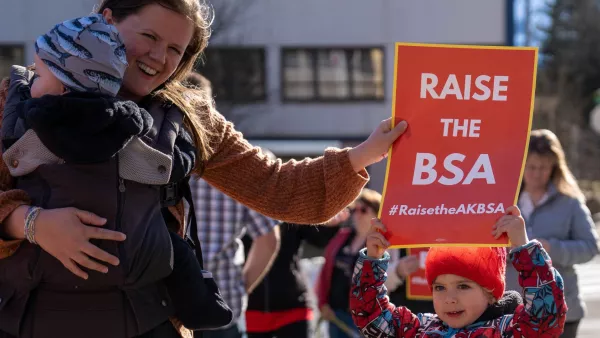 A member holding a baby helps one of her children hold a sign that says "Raise the BSA"