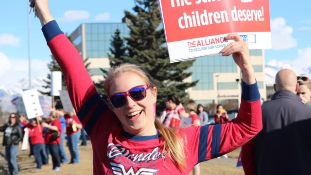 A person with a long blonde pony-tail wearing a Wonder Woman shirt cheers.