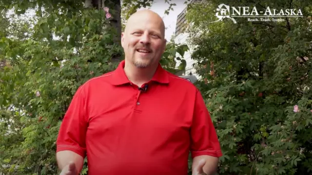 Tom Klaameyer smiling in a red shirt in front of foliage