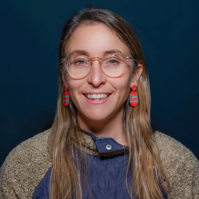 A woman posing for a portrait with clear glasses and big red earrings.