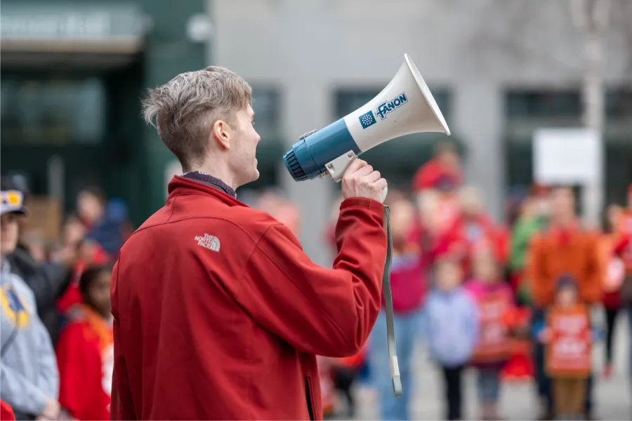 A man in red speaking into a megaphone in front of a crowd